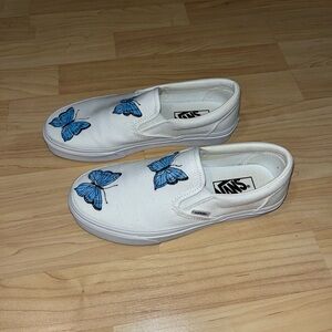 White slip on vans with painted on blue butterflies